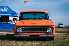 an orange truck parked on top of a grass covered field next to a blue tent