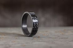 a wedding band with black carbon fiber inlaying the center, on a concrete surface