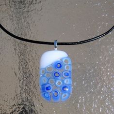 a blue and white glass bead hangs from a black cord on the sand at the beach