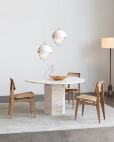 a white table with chairs and a bowl on it in front of two lamps hanging from the ceiling