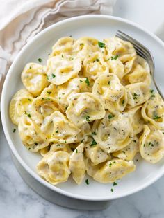 a white bowl filled with pasta covered in sauce and garnished with parsley