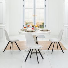 a white dining room table with four chairs and plates on the table in front of it