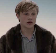 a young man in a fur coat looking at the camera