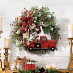 a christmas wreath with a red truck and evergreens is hung on the wall next to candles