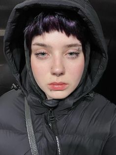 a young woman with purple hair wearing a black jacket and hood over her head is staring at the camera