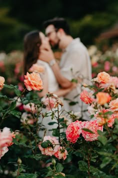 a man and woman are kissing in the middle of some pink flowers with their faces close to each other