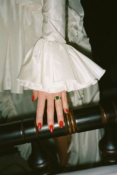 a woman's hand with red fingernails and ring on top of a rail in front of her wedding dress