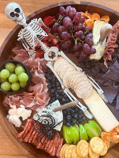 a wooden platter filled with cheese, crackers, fruit and skeleton figurines