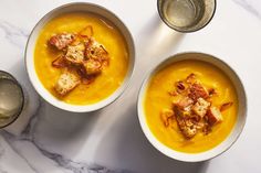 two bowls filled with soup and bread on top of a white table next to silver cups