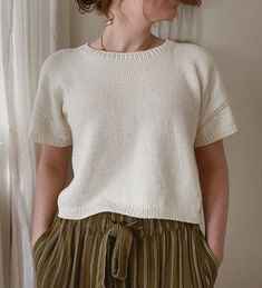 a woman standing in front of a window wearing a white sweater and green pleated skirt