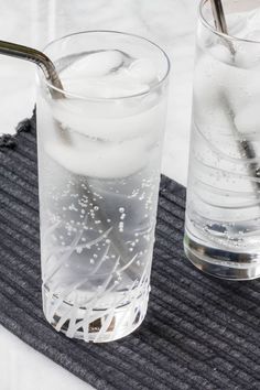 two glasses filled with water and ice on top of a mat next to each other