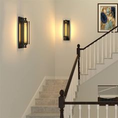 a staircase with two lights on each side and pictures on the wall next to it