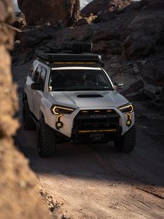 a white suv driving down a dirt road next to rocks and boulders in the desert