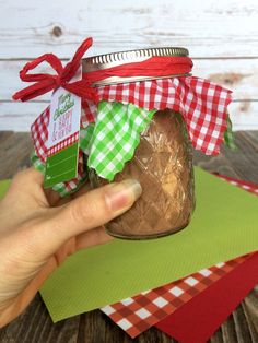 a hand holding a jar filled with food on top of paper and red checkered ribbon