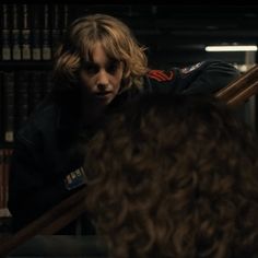 a man with long blonde hair sitting in front of a book shelf next to a woman