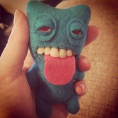 a hand holding a small green monster with red tongue and teeth on it's face