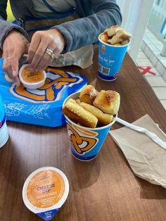 a person sitting at a table with two cups of food in front of them and one cup filled with ice cream