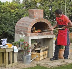 a man in an apron is cooking food on the outdoor brick pizza oven with potted plants