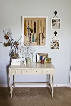 a white table topped with lots of jewelry next to a wall filled with framed pictures