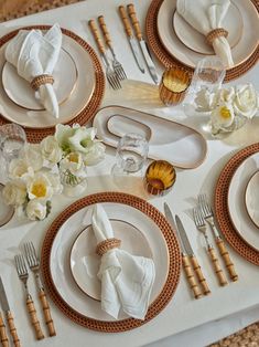 the table is set with gold and white plates, silverware, napkins, and flowers