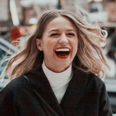 a woman laughing while walking down the street with her hair blowing in the wind and she is wearing a black coat