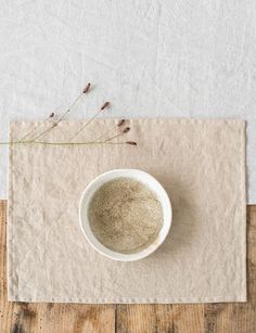 a white bowl filled with some kind of substance on top of a wooden table next to a plant