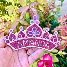 a hand holding a pink princess tiara with the word amanda on it