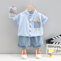 Toddler Boy Pocket T-shirt & Striped Shorts Wholesale Children's Clothing - PrettyKid Light Blue Cotton Sets For Summer, Light Blue Short Sleeve Sets For Summer, Light Blue Short Sleeve Summer Sets, Light Blue Cotton Short Sleeve Sets, Light Blue Short Sleeve Sets For Spring, Light Blue Short Sleeve Spring Sets, Playful Light Blue Cartoon Print Sets, Cotton Sets With Cartoon Print For Playtime, Cute Blue Cotton Set