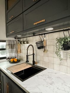 a kitchen sink with hanging utensils on the wall next to it and some oranges