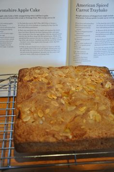 an open book sitting on top of a cooling rack next to a baked cake covered in nuts