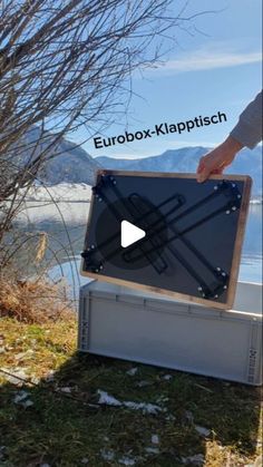 a person is holding a large box in front of some water and trees with the words eurobox klappissch on it