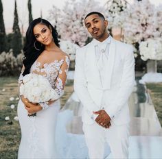 a man and woman standing next to each other in front of some trees with white flowers