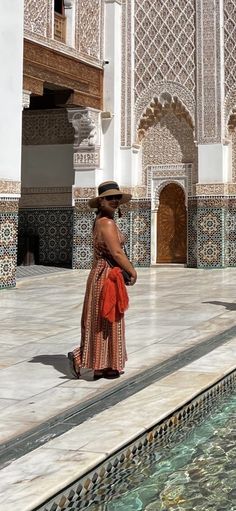 a woman is standing in front of a pool and looking at the building's architecture