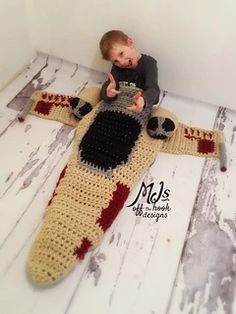 a little boy sitting on top of a crocheted jesus figure with his thumb up