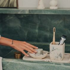 a woman's hand reaching for a toothbrush in a marbled bathroom sink