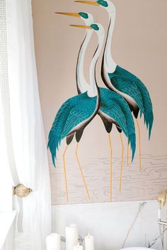 two large blue birds are standing in the bathtub next to candles and a painting on the wall