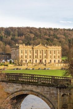 an old stone bridge crossing over a river in front of a large building on a hill