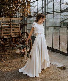 a woman in a white dress standing next to a wheelbarrow with flowers on it