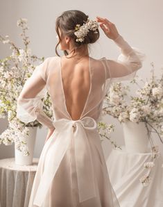 the back of a woman's dress, with her hands on her head and flowers behind her