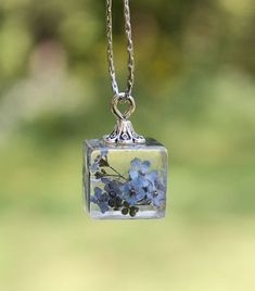 a glass pendant with blue flowers hanging from it's side on a silver chain