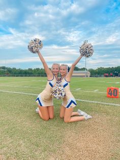 two cheerleaders kneeling on the ground with their hands in the air