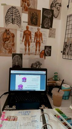 an open laptop computer sitting on top of a white desk covered in medical diagrams and drawings