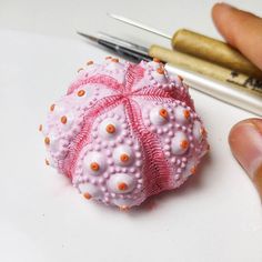 a pink bead ball with orange dots is being held by someone's hand