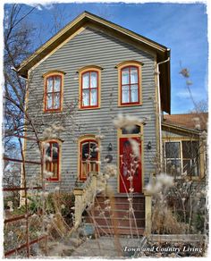 an old gray house with red trim and two story windows on the second floor is surrounded by tall grass