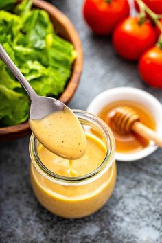 a spoon full of dressing sitting on top of a table next to tomatoes and lettuce