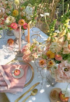 the table is set with pink and yellow flowers in vases, plates, napkins and candles