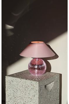 a pink table lamp sitting on top of a block of cement next to a wall