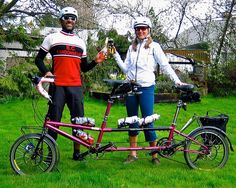 two people standing next to each other holding beers and bicycles in front of their faces