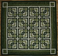 a green and white quilt with squares in it on a wooden floor next to a wall