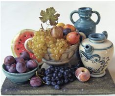 there are many different types of fruit in the bowl and vases on the table